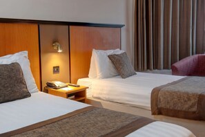 Two single beds with white linens and brown headboards, each with a bedside table and telephone.