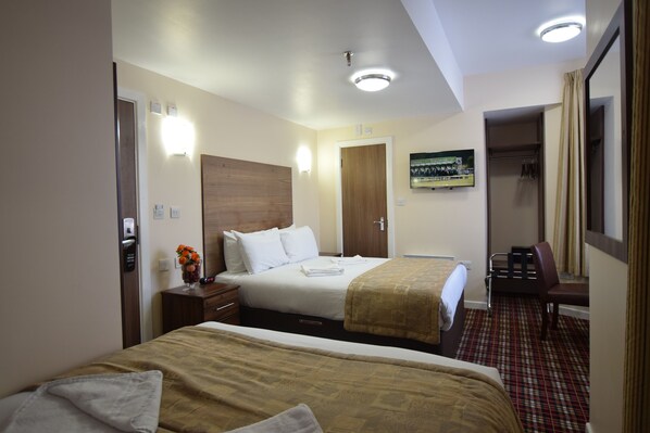 Two beds with neatly made linens and a large mirror above, complemented by a small table and a vase of flowers.