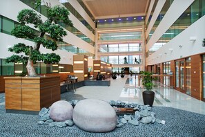 Experience the grandeur of our lobby, featuring a high ceiling, large windows, and a central seating area with a reception desk.