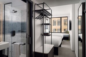 Enjoy a city view from the large windows, with a compact bed area and a small bedside table featuring a plant.