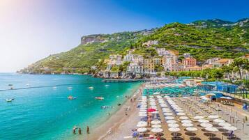 Relax on the beach with comfortable sun loungers and umbrellas, surrounded by calm waters and scenic cliffside architecture.